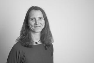 Schwarz-weiß-Porträt einer Person mit schulterlangem Haar, die ein schlichtes Oberteil und eine Halskette trägt.