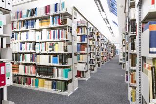 Ein langer Gang in der Bibliothek ist zu sehen, auf beiden Seiten zahlreiche Bücherregale, an der Decke eine Dachschräge mit Dachfenstern
