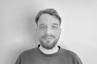 Person mit kurzem Haar und Bart trägt ein Sweatshirt vor einfarbigem Hintergrund