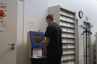 Eine Person steht in der Bibliothek des GWZO am Selbstverbuchungsautomaten und leiht ein Buch aus.