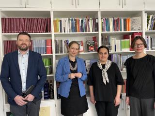 Vier Personen stehen vor einem Bücherregal, von links nach rechts: Bálint Kovács in dunklem Anzug, Maren Röger in blauem Blazer und schwarzem Kleid, Edita Gzoyan in schwarzem Oberteil mit gemustertem Halstuch, Katja Castryck-Naumann in schwarzem Pullover.