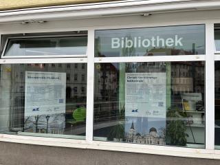 Fensterfront einer Bibliothek mit zwei großen Informationsplakaten zu Skowrodo-Museum und Christi-Verklärungs-Kathedrale.