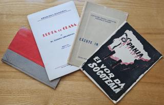 Vier alte Bücher liegen auf einem Holztisch, eines mit rotem und grauem Einband, die anderen mit bedruckten Umschlägen in verschiedenen Farben.