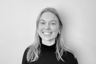 Person mit langen Haaren, die einen schwarzen Rollkragenpullover trägt, vor weißem Hintergrund.