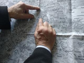 Zwei Hände zeigen auf einen schwarz-weißen Stadtplan von Lviv mit Ortsnamen und Straßenverläufen.