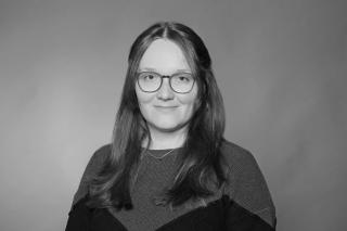 Portrait schwarz weiß: Frau mit langen Haaren, vor einfarbigem Hintergrund.