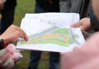 Mehrere Personen betrachten einen farbigen Lageplan mit Gebäuden und Grünflächen, eine Hand zeigt auf den Plan.