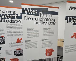 Drei aufgestellte Roll-ups mit Texten und Fotos zu Dissidenz und Befürchtungen von Dissident*innen in einem Innenraum.