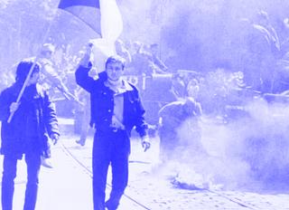 Schwarz-weiß-Fotografie einer Demonstration mit mehreren Personen, von denen eine eine Fahne hält, und Rauch auf der Straße