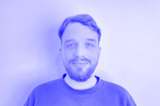 Person mit kurzem Haar und Bart trägt ein Sweatshirt vor einfarbigem Hintergrund