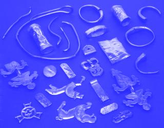 Eine Anordnung von verschiedenen silbernen Schmuckstücken, darunter Ringe, Anhänger, und verzierte Platten, auf einem blauen Untergrund.