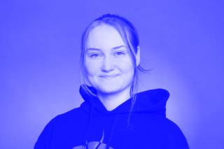 Person mit zusammengebundenem Haar trägt schwarzen Kapuzenpullover vor einfarbigem Hintergrund.