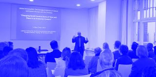 Vortragender steht vor einem Publikum in einem hellen Raum mit großen Fenstern und präsentiert eine Folie mit dem Titel 'Global Armenia/NS: The Entangled Histories of Central and Eastern Europe and the Caucasus'