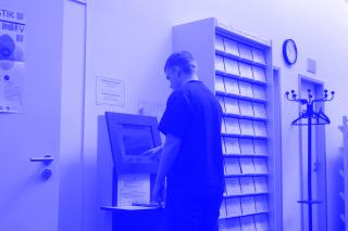 Eine Person steht in der Bibliothek des GWZO am Selbstverbuchungsautomaten und leiht ein Buch aus.