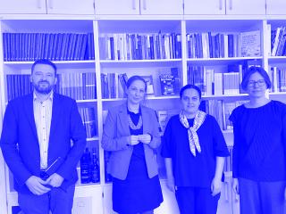 Vier Personen stehen vor einem Bücherregal, von links nach rechts: Bálint Kovács in dunklem Anzug, Maren Röger in blauem Blazer und schwarzem Kleid, Edita Gzoyan in schwarzem Oberteil mit gemustertem Halstuch, Katja Castryck-Naumann in schwarzem Pullover.