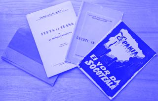 Vier alte Bücher liegen auf einem Holztisch, eines mit rotem und grauem Einband, die anderen mit bedruckten Umschlägen in verschiedenen Farben.