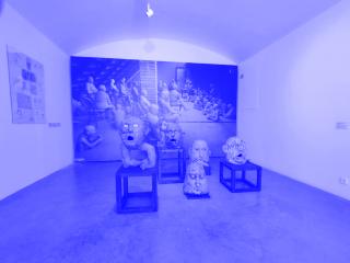 Ausstellung mit mehreren Skulpturen von Köpfen und Figuren auf Holzpodesten vor einer Wand mit großem Schwarz-Weiß-Foto von sitzenden Figuren