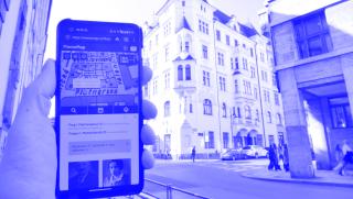 Ruka drží mobilní telefon s mapou před budovou, ve které se nachází GWZO v Praze. Název: Na cestách po Praze s aplikací Memo (c) Michal Frankl