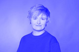 Person mit kurzem Haar trägt einen Pullover mit Rundhalsausschnitt vor einfarbigem Hintergrund