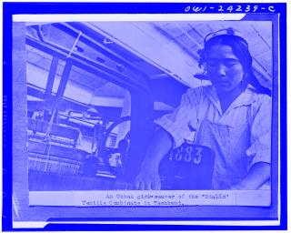 Schwarz-weiße Fotografie einer Frau an einem Webstuhl in einer Textilfabrik.