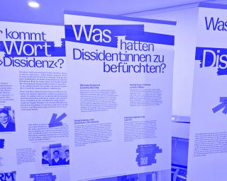 Drei aufgestellte Roll-ups mit Texten und Fotos zu Dissidenz und Befürchtungen von Dissident*innen in einem Innenraum.