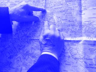 Dvě ruce ukazují na černobílý plán města Lvov s názvy míst a trasami ulic.