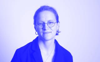 Schwarz-weiße Porträtaufnahme einer Person mit Brille, Ohrringen und zurückgebundenem Haar, die leicht lächelt.