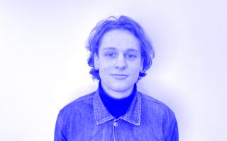 Person trägt Jeansjacke über dunklem Rollkragenpullover vor weißem Hintergrund.