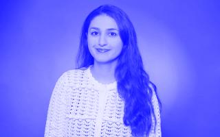 Person mit langen, welligen Haaren trägt eine weiße, gehäkelte Bluse vor einfarbigem Hintergrund