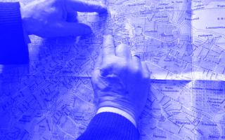 Zwei Hände zeigen auf einen schwarz-weißen Stadtplan von Lviv mit Ortsnamen und Straßenverläufen.