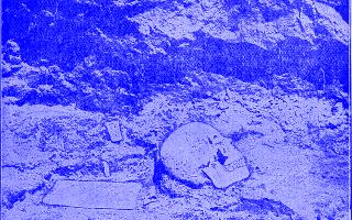 Schwarz-weiße Aufnahme eines menschlichen Schädels, der teilweise im Boden vergraben liegt, umgeben von Erdschichten.