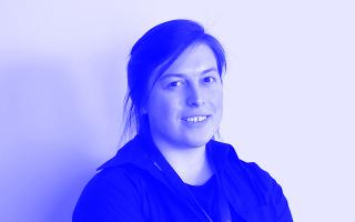 Schwarz-weiß-Porträt einer Person mit zusammengebundenem Haar und schwarzem Hemd vor hellem Hintergrund.