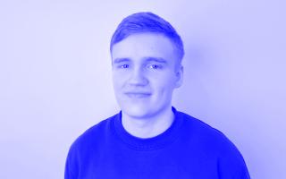 Schwarz-weiß-Porträt einer Person mit kurzem Haar und Pullover vor einfarbigem Hintergrund