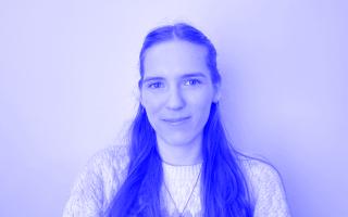 Portrait von Person mit langem, glattem Haar, die einen Pullover und eine Halskette trägt, vor einfarbigem Hintergrund, schwarz-weiß.