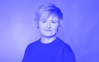 Person mit kurzem Haar trägt einen Pullover mit Rundhalsausschnitt vor einfarbigem Hintergrund