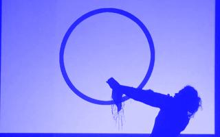 Schattenriss einer Person mit ausgebreitetem Arm vor einem blauen Hintergrund und einem schwarzen Kreis, Szene aus dem Theaterstück 'I Declare' (2011) von Alina Șerban.