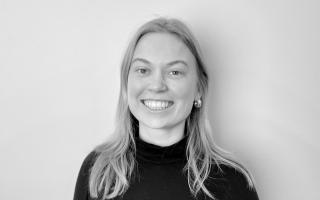 Person mit langen Haaren, die einen schwarzen Rollkragenpullover trägt, vor weißem Hintergrund.