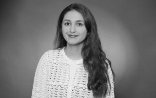 Person mit langen, welligen Haaren trägt eine weiße, gehäkelte Bluse vor einfarbigem Hintergrund