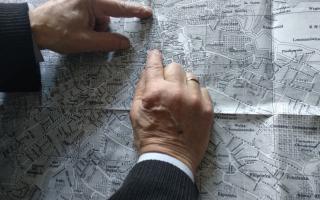 Zwei Hände zeigen auf einen schwarz-weißen Stadtplan von Lviv mit Ortsnamen und Straßenverläufen.