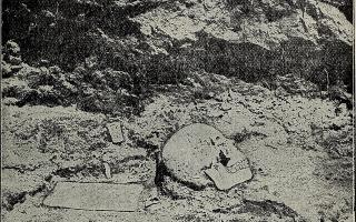 Schwarz-weiße Aufnahme eines menschlichen Schädels, der teilweise im Boden vergraben liegt, umgeben von Erdschichten.