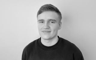 Schwarz-weiß-Porträt einer Person mit kurzem Haar und Pullover vor einfarbigem Hintergrund